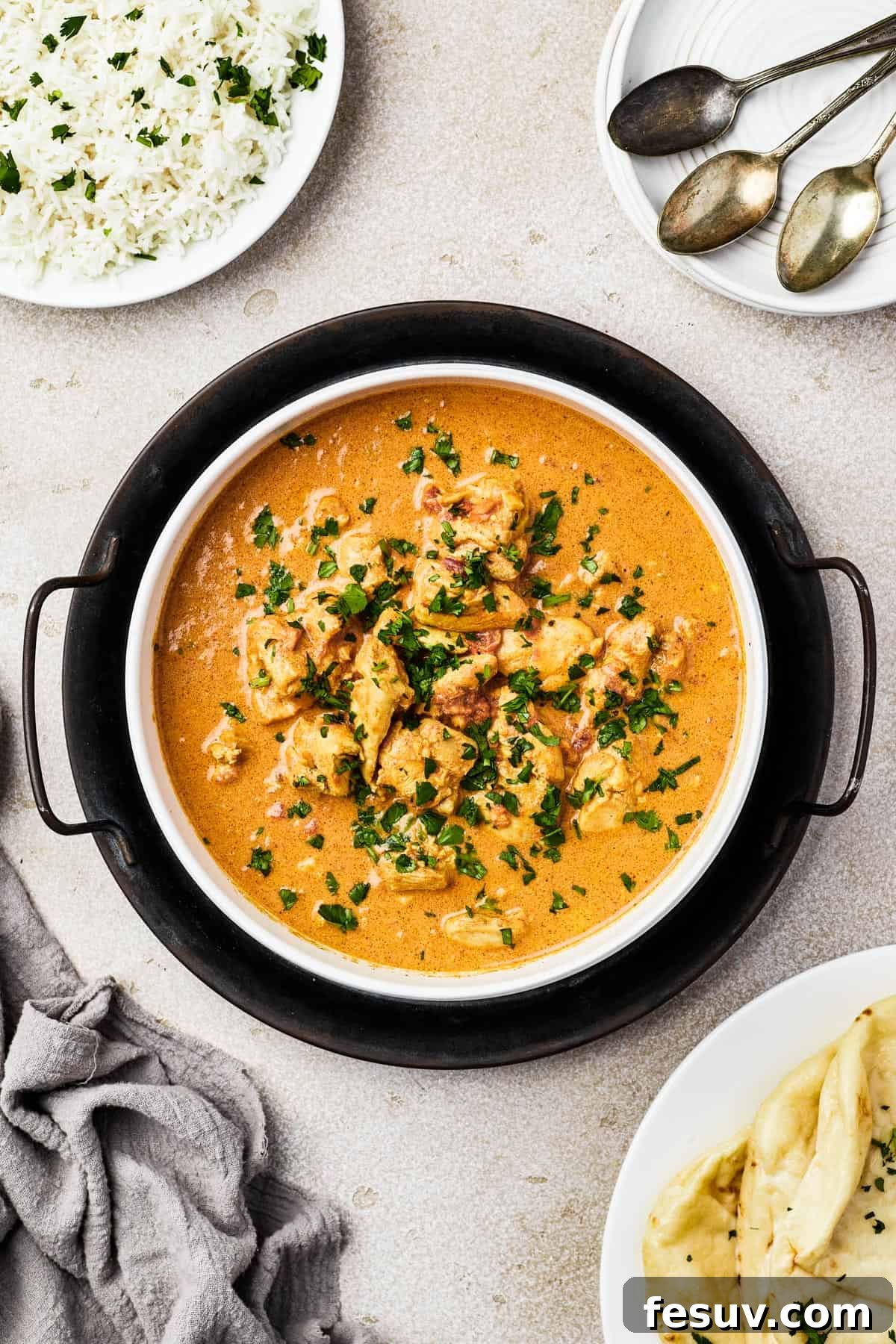 Overhead shot of a white enamel dish, resting on a cast-iron holder. The dish is filled with butter chicken, garnished with cilantro.