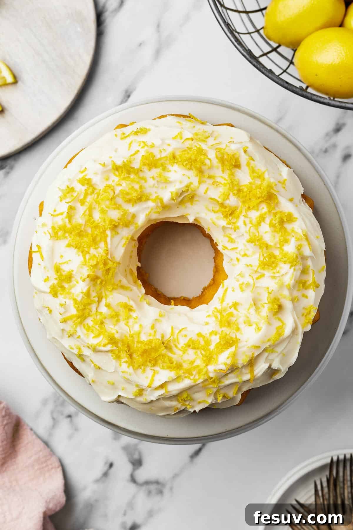 Zesty Lemon Bundt Delight 7 A decorated cake with white frosting and lemon zest on a round white plate.