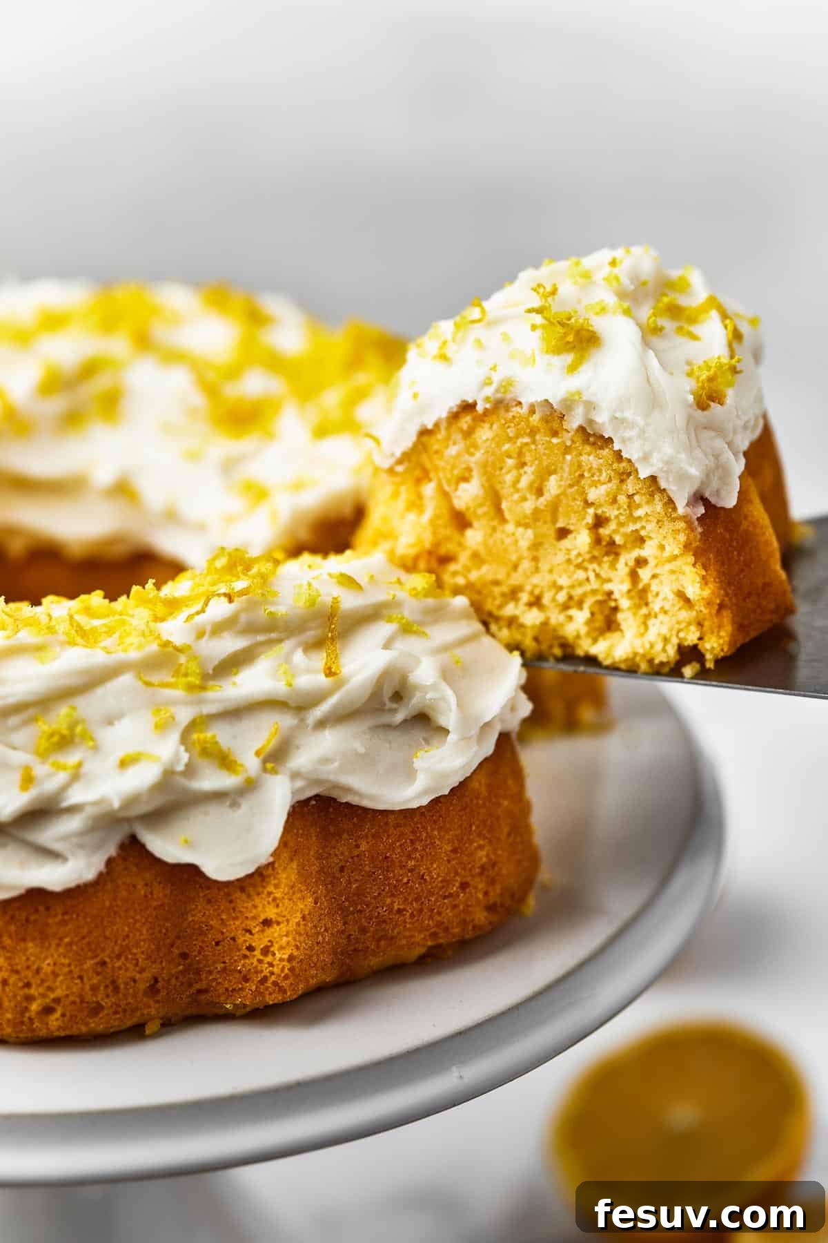 Zesty Lemon Bundt Delight 8 A Bundt cake on a platter, with one slice being removed on a cake server.