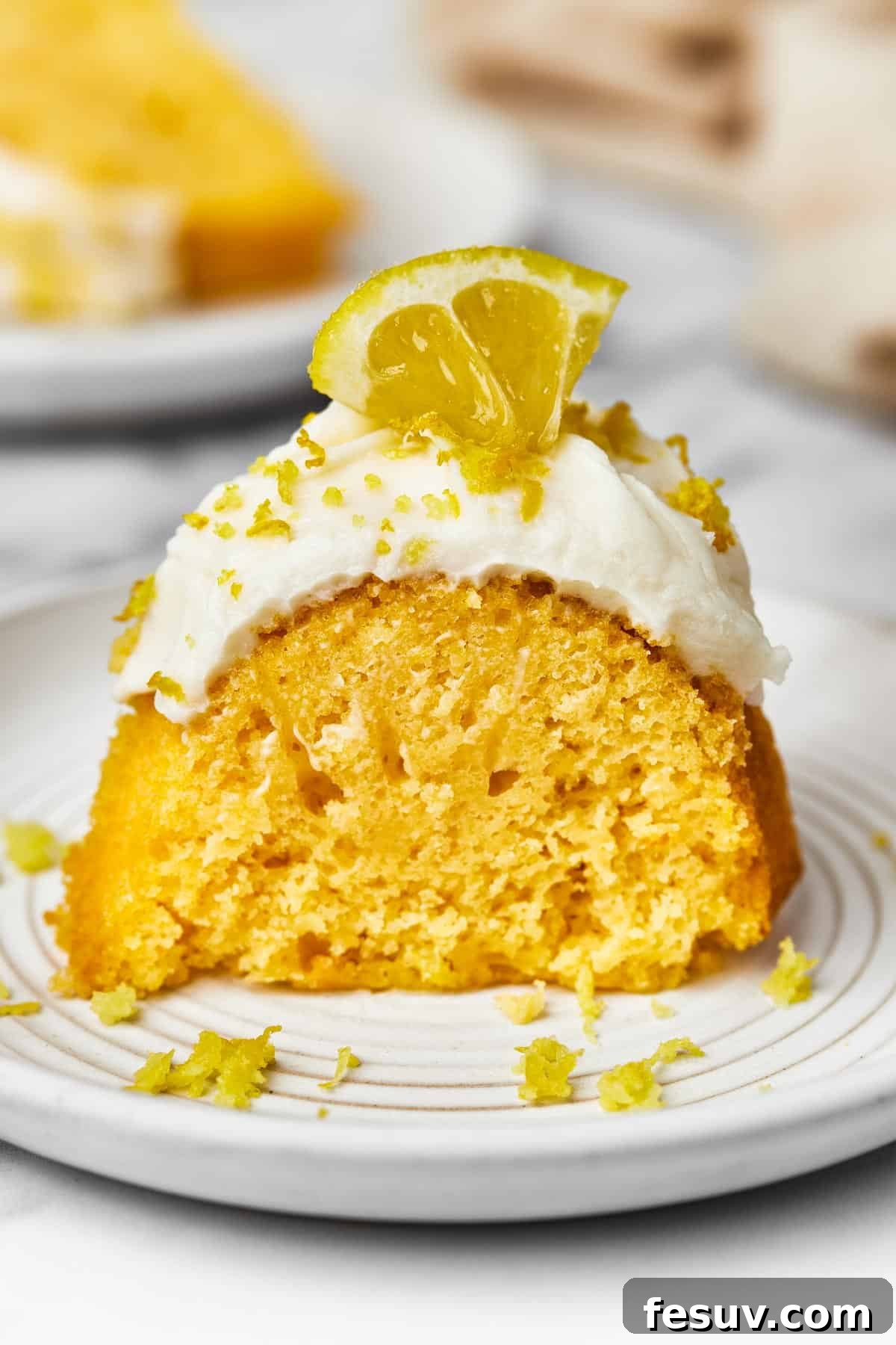 Zesty Lemon Bundt Delight 9 A slice of frosted cake, garnished with lemon zest and a small lemon wedge.