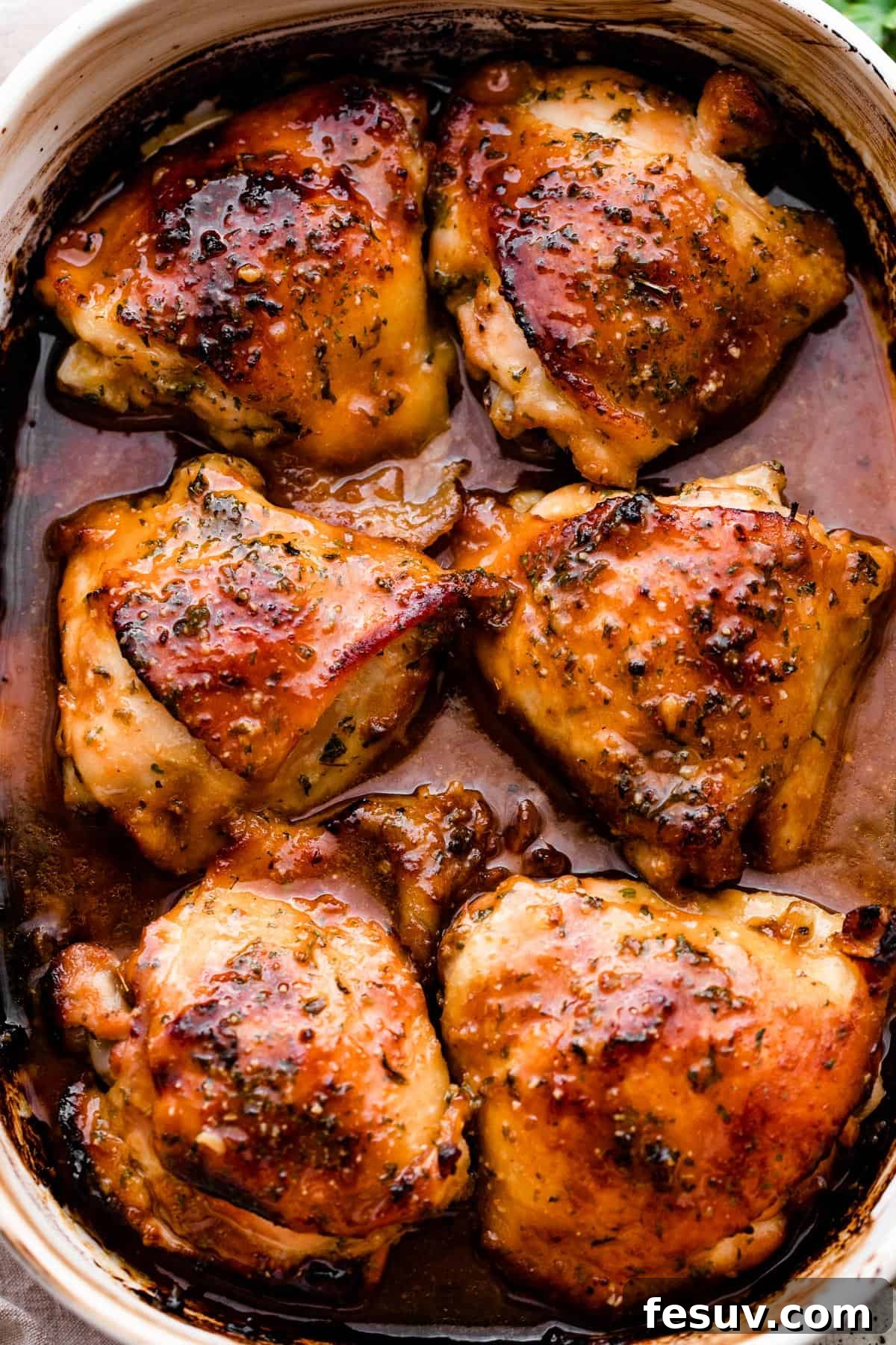 Overhead shot of a white ceramic baking dish brimming with six perfectly baked honey garlic chicken thighs, showing off their golden-brown, crispy skin and sticky glaze.