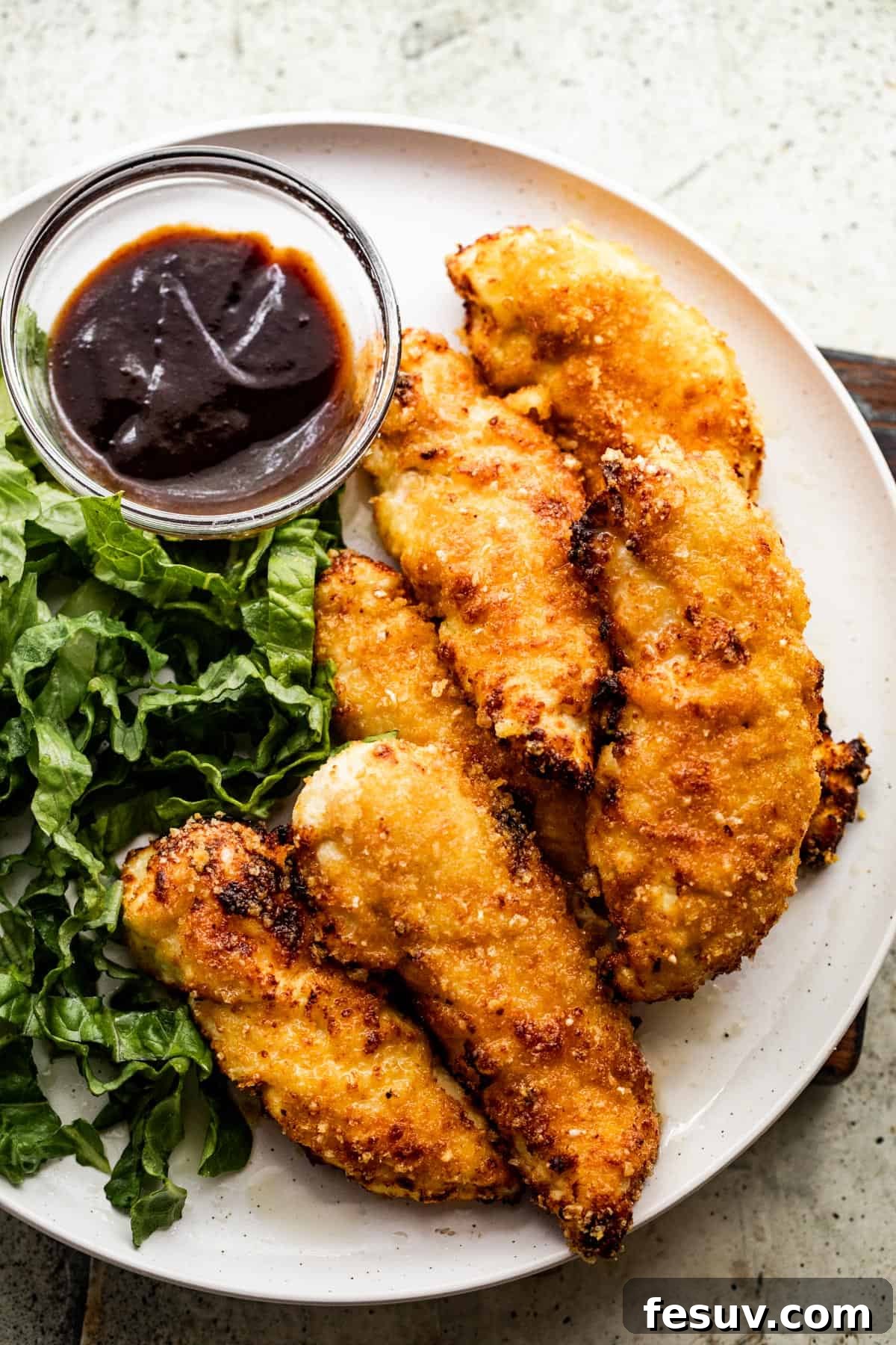 Restaurant Quality Crispy Air Fryer Chicken 2 An overhead shot of a dinner plate featuring golden-brown air fryer chicken tenders, a vibrant green salad, and a ramekin of BBQ sauce.
