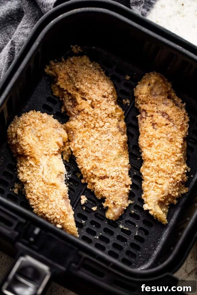 Restaurant Quality Crispy Air Fryer Chicken 5 Three raw breaded chicken tenders perfectly arranged in a single layer inside a black air fryer basket, ready for cooking.