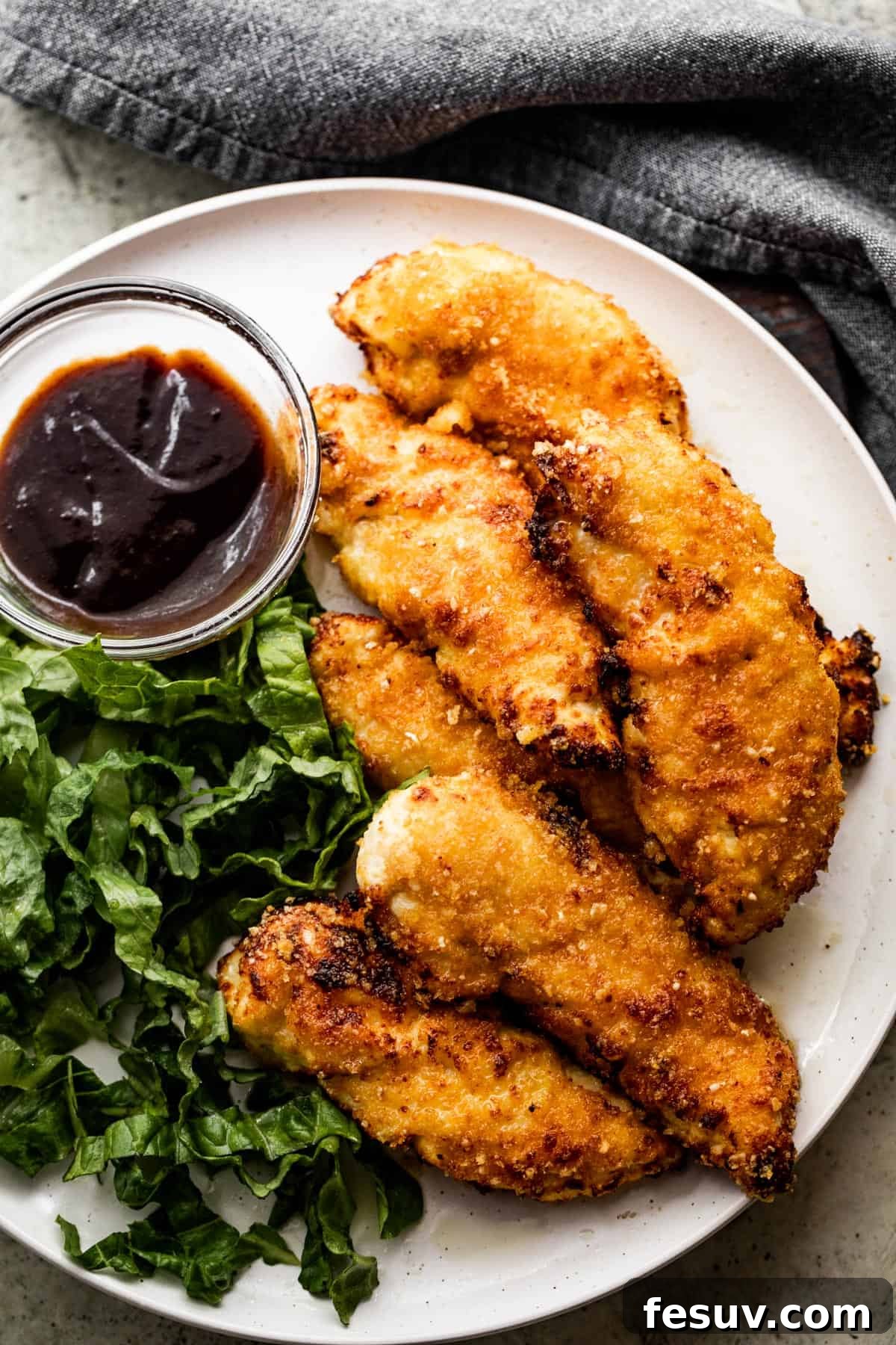 Restaurant Quality Crispy Air Fryer Chicken 7 A beautifully presented dinner plate featuring crispy air fryer chicken tenders, a fresh green side salad, and a ramekin of rich BBQ sauce.