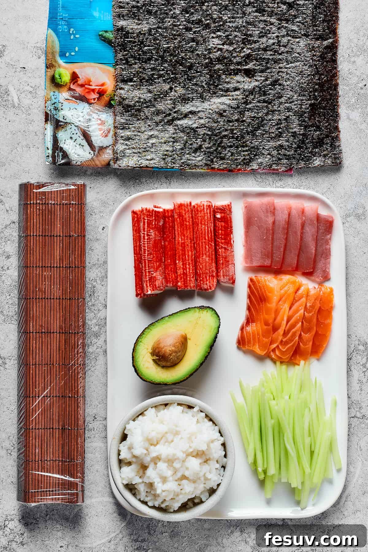 Rainbow Sushi Masterpiece 4 From top: Sheets of nori, a bamboo sushi mat, sticks of imitation crab, sliced raw tuna, an avocado, sliced raw salmon, prepared sushi rice, and sliced cucumber.