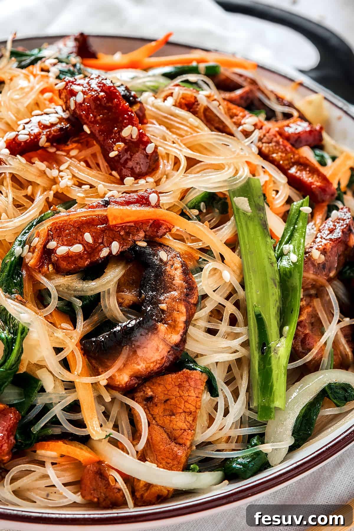 A shallow dish of beef noodle stir fry, garnished with sesame seeds.