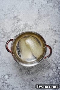 Glass noodles rehydrating in a stainless steel pot of hot water.
