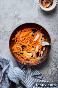 Matchstick carrots and sliced onions in a skillet.