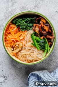 A large bowl with glass noodles, beef, mushrooms, green onions, carrots, and spinach.