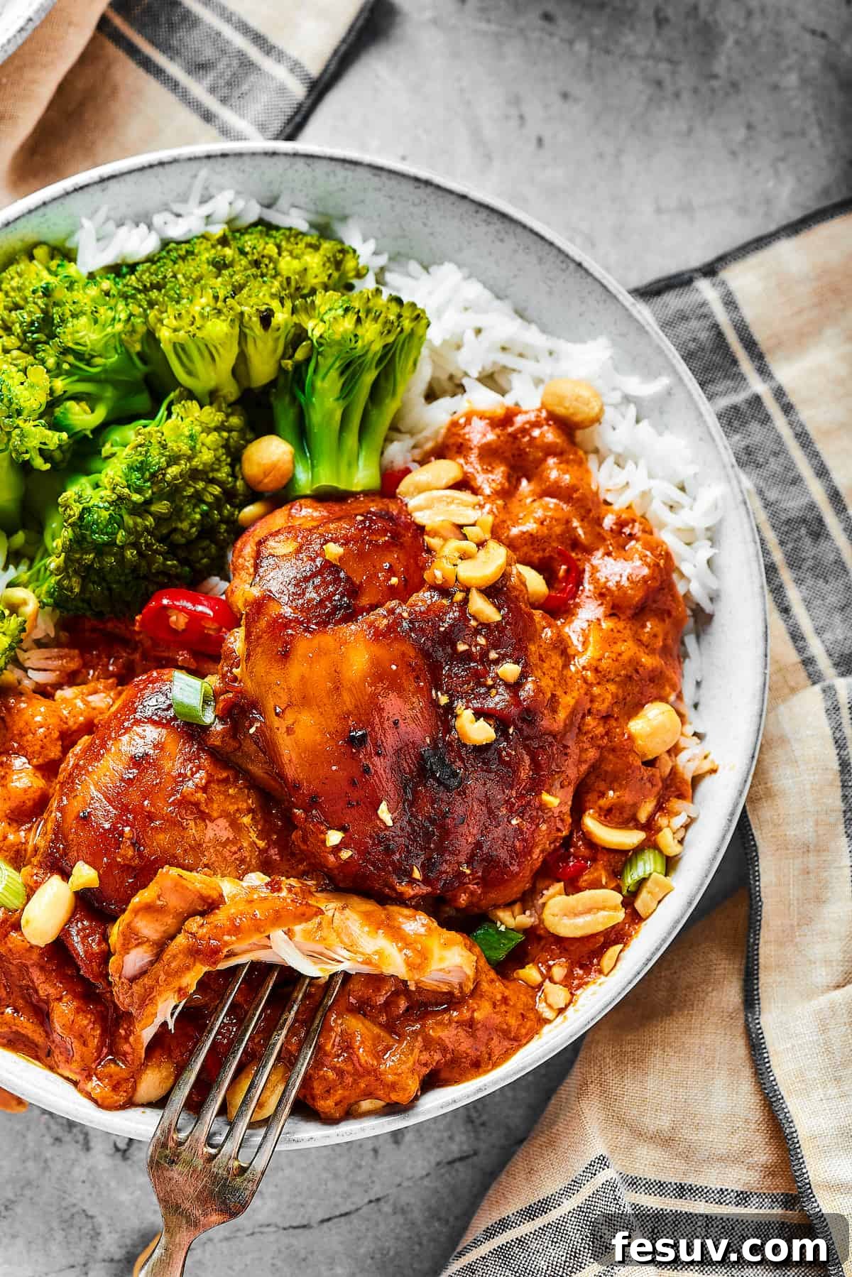 Simple Peanut Butter Chicken with crushed tomatoes, soy sauce, and garlic is a breeze to make. Serve this saucy chicken over rice, noodles, or cauliflower rice, and watch it disappear! overhead shot of a chicken thigh cooked in peanut sauce, with a fork pulling away a bite.