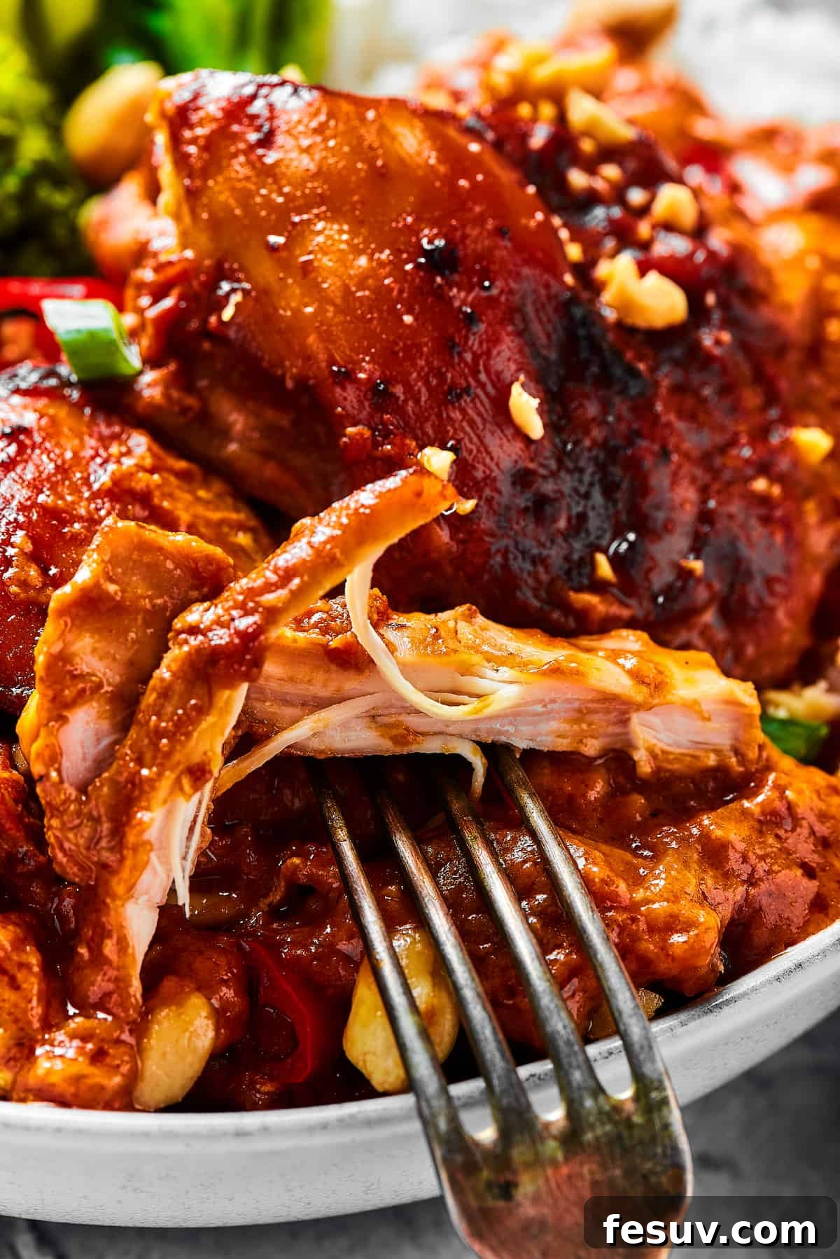 Simple Peanut Butter Chicken with crushed tomatoes, soy sauce, and garlic is a breeze to make. Serve this saucy chicken over rice, noodles, or cauliflower rice, and watch it disappear! A close-up shot of a chicken thigh cooked in peanut sauce, with a fork pulling away a bite.