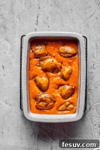 Velvety Peanut Butter Chicken 7 A baking dish full of creamy tomato peanut sauce, with chicken thighs arranged in the sauce.