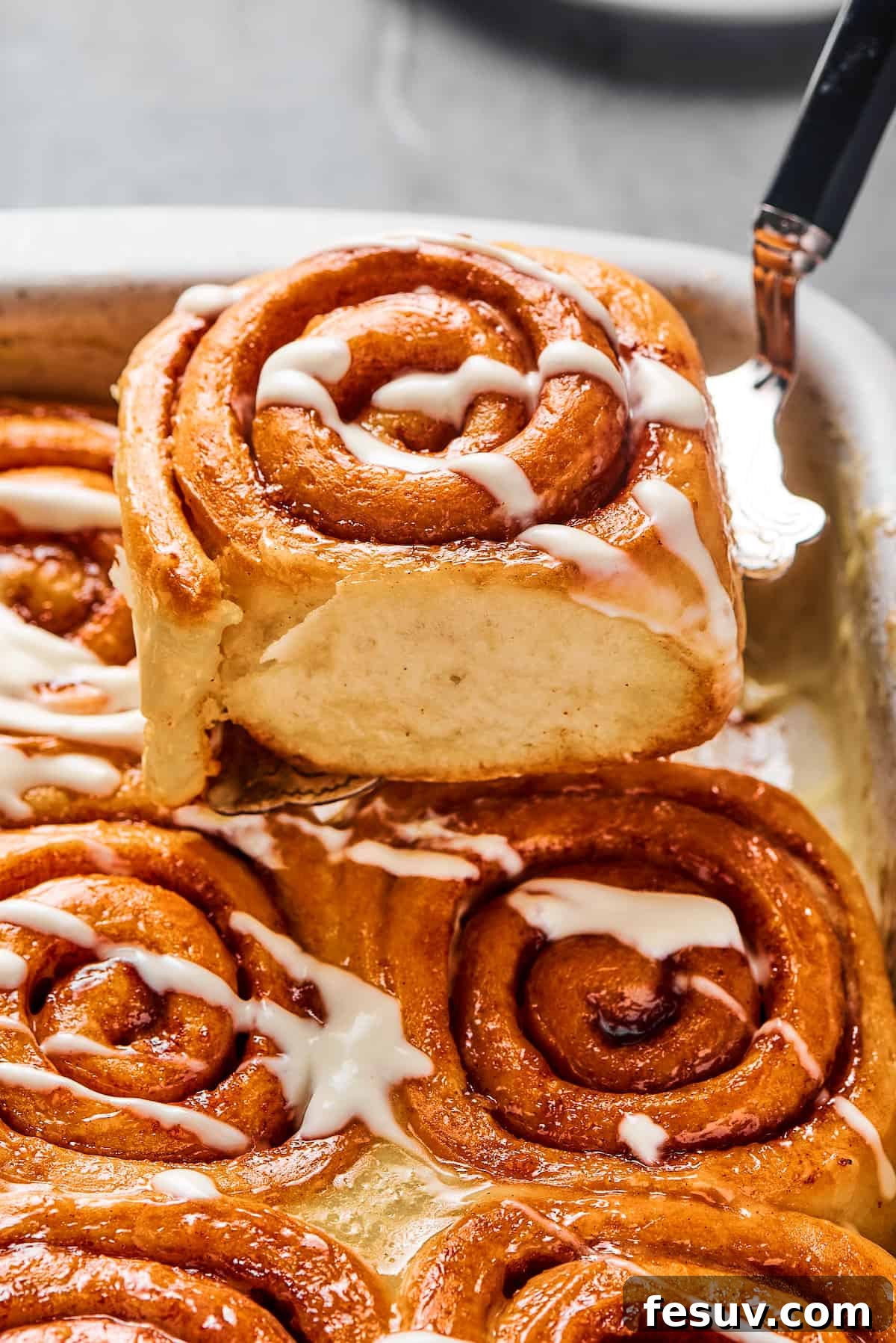 A cinnamon bun lifted from a pan, to show the texture of the torn side of the roll.