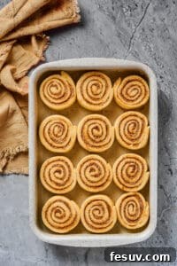 Sliced, unbaked cinnamon buns, lined up in a metal baking dish.