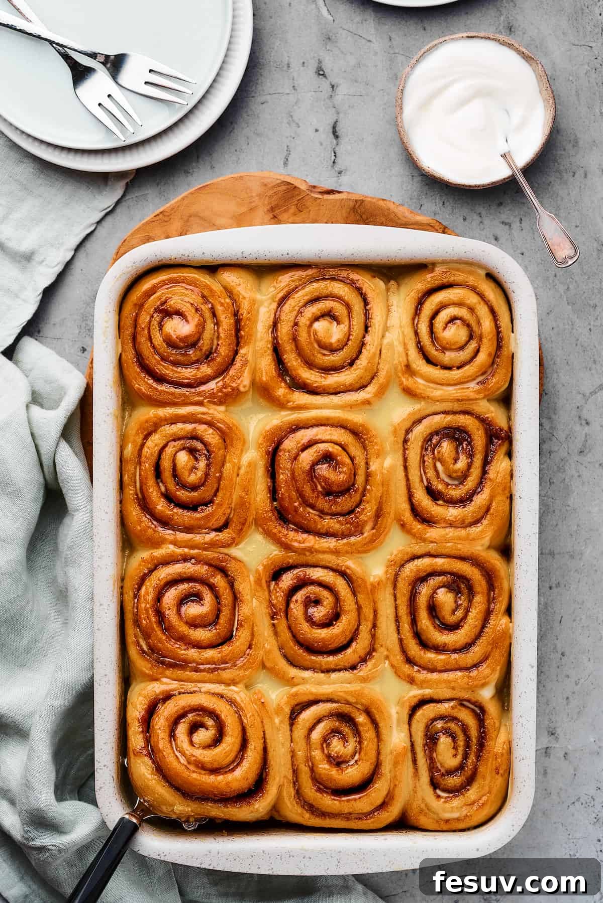 Baked cinnamon rolls in a baking pan, with a cloth dishtowel nearby.