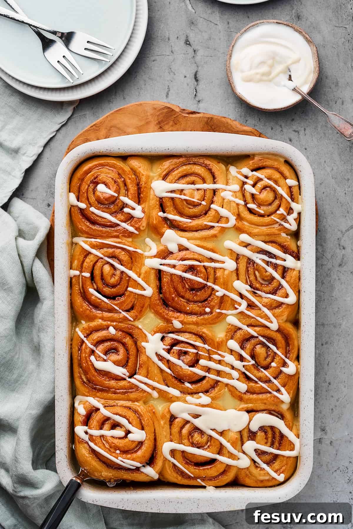 A pan of baked cinnamon rolls drizzled with icing.