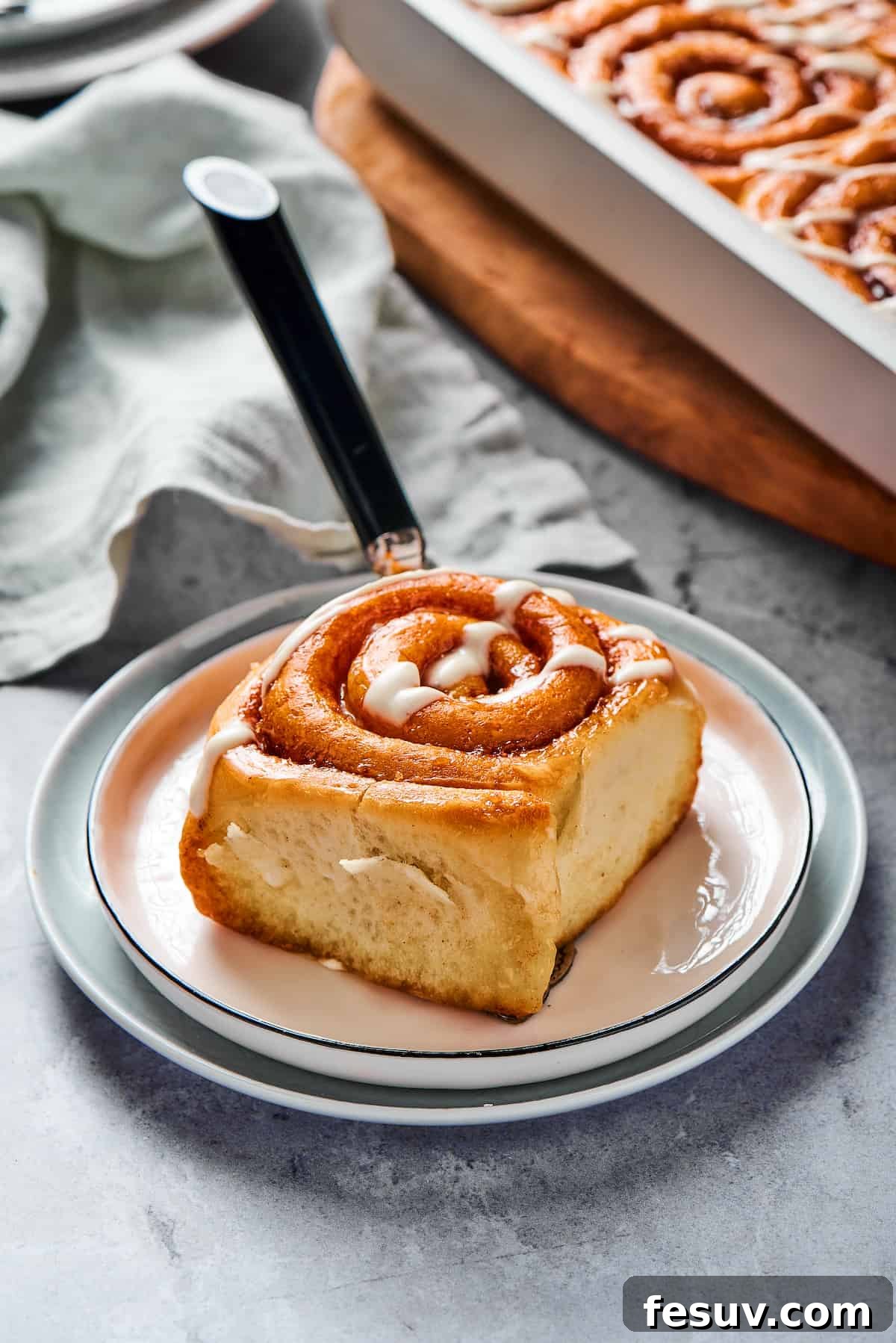 A single sticky roll on a small plate, with a fork and a cloth napkin.