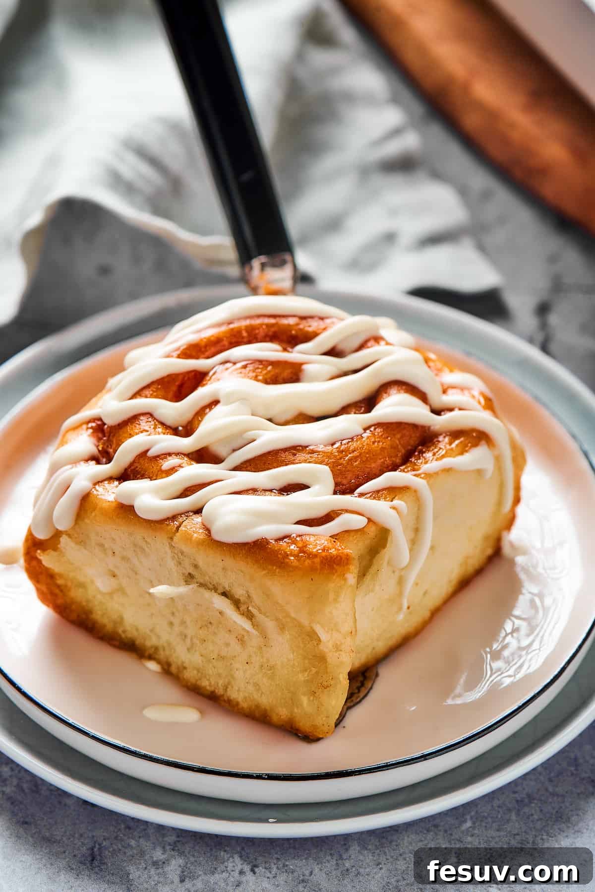A fresh cinnamon bun on a small plate, with thick white glaze drizzled on top.