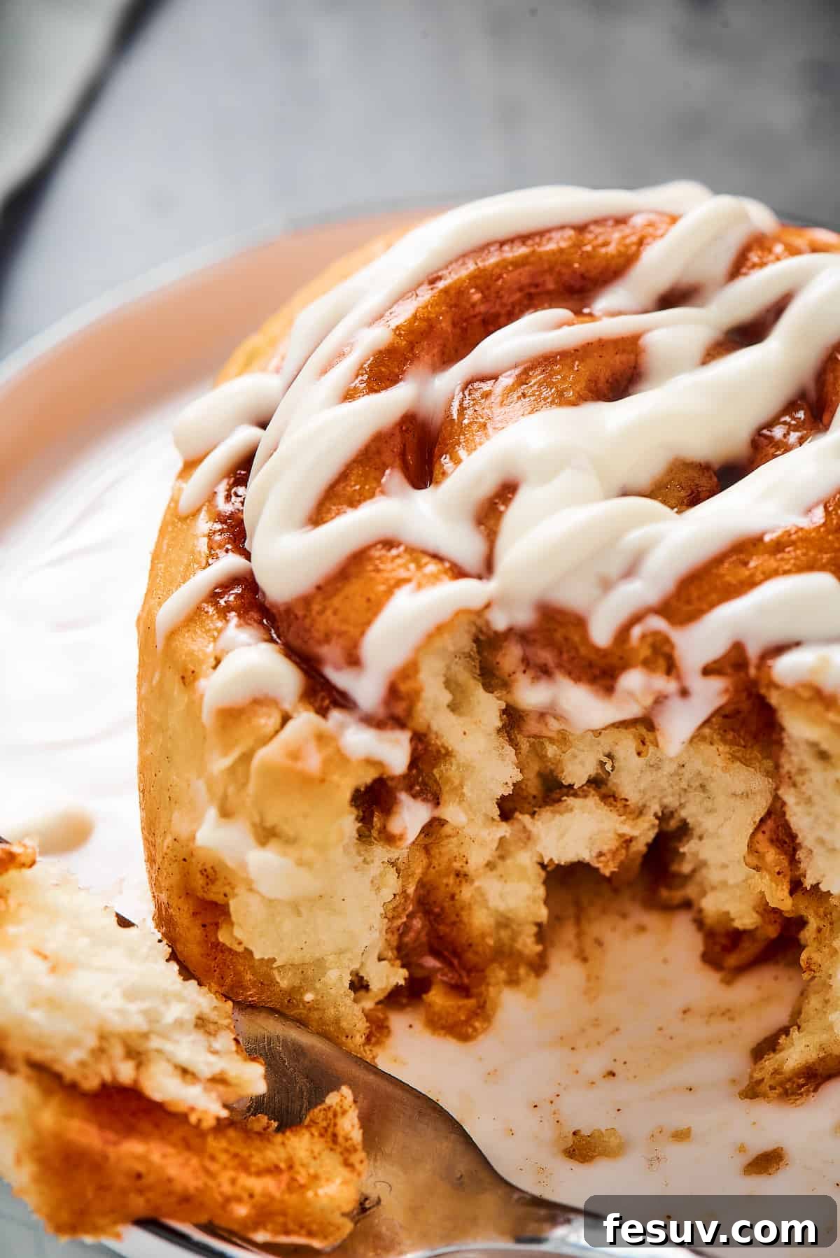 A fresh cinnamon roll with a bite taken from it, on a small plate.