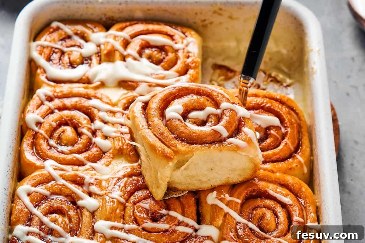 One sticky roll iced with a drizzle of glaze, sitting on the pan of rolls.