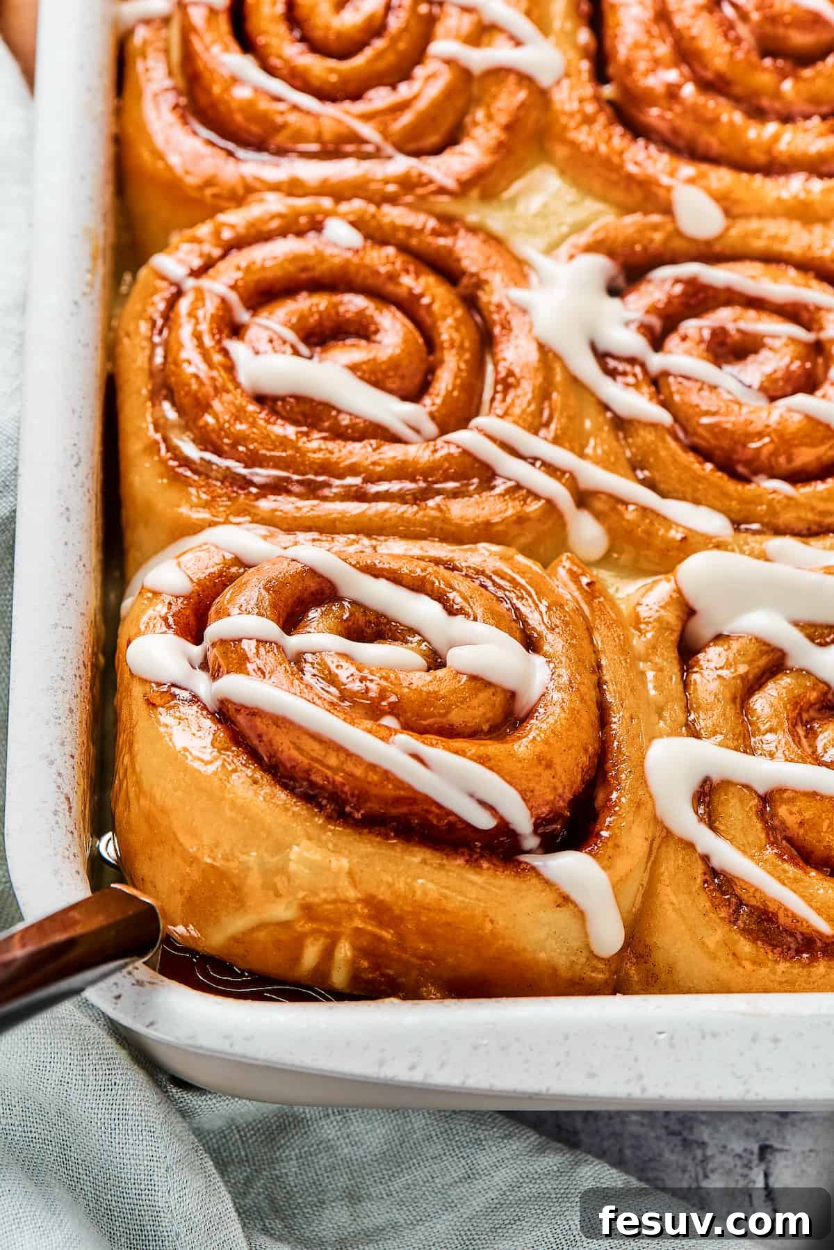 A pan of sticky homemade cinnamon buns. One is being lifted from the corner of the pan with a metal spatula.
