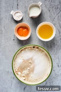 Dry baking ingredients mixed in a large mixing bowl. Sugar, milk, egg yolks, and melted butter are near the bowl in separate dishes.