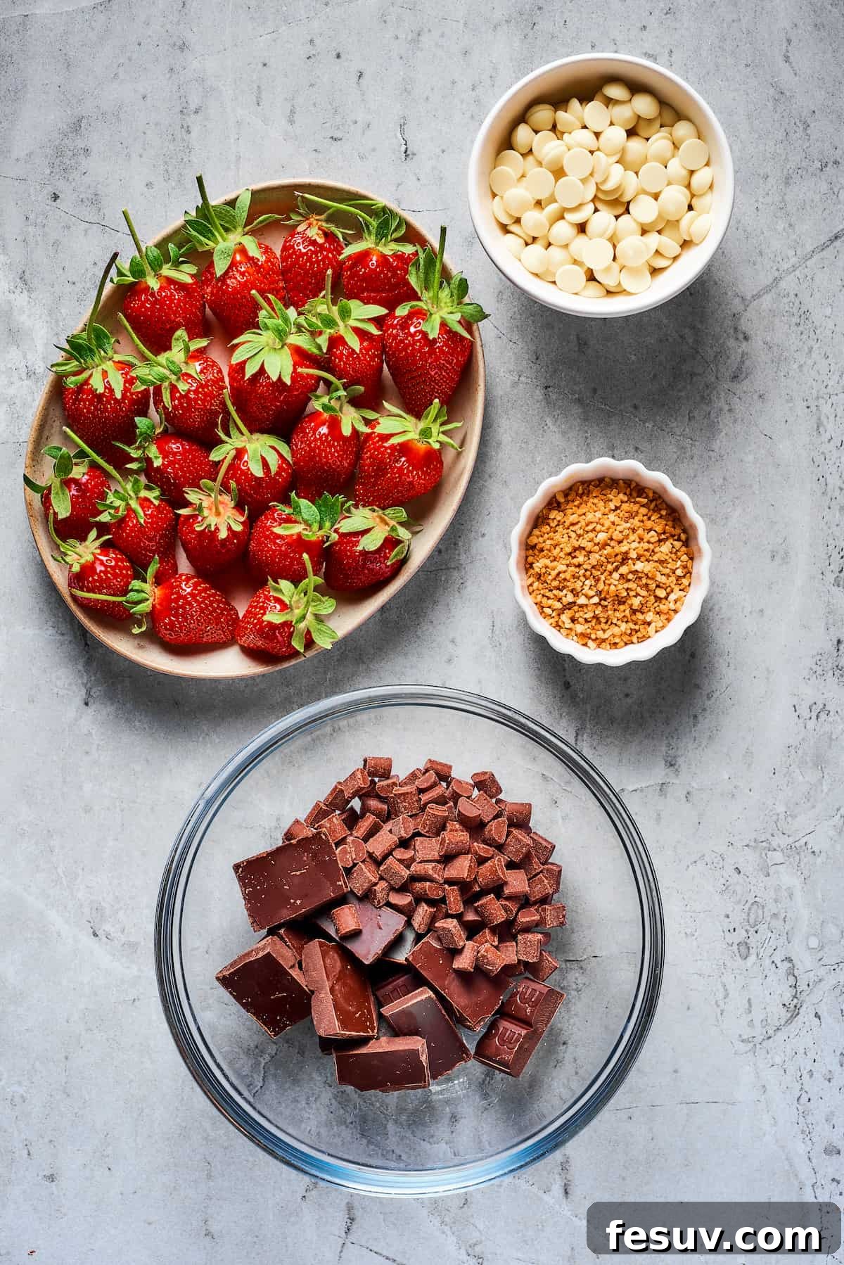 Essential Ingredients for Delicious Chocolate Covered Strawberries Four bowls on a table, displaying ingredients for chocolate-covered strawberries. From top left, clockwise: fresh strawberries with vibrant green stems, white chocolate chips, toasted chopped hazelnuts, and a bowl containing a mix of semisweet chocolate and milk chocolate chips.