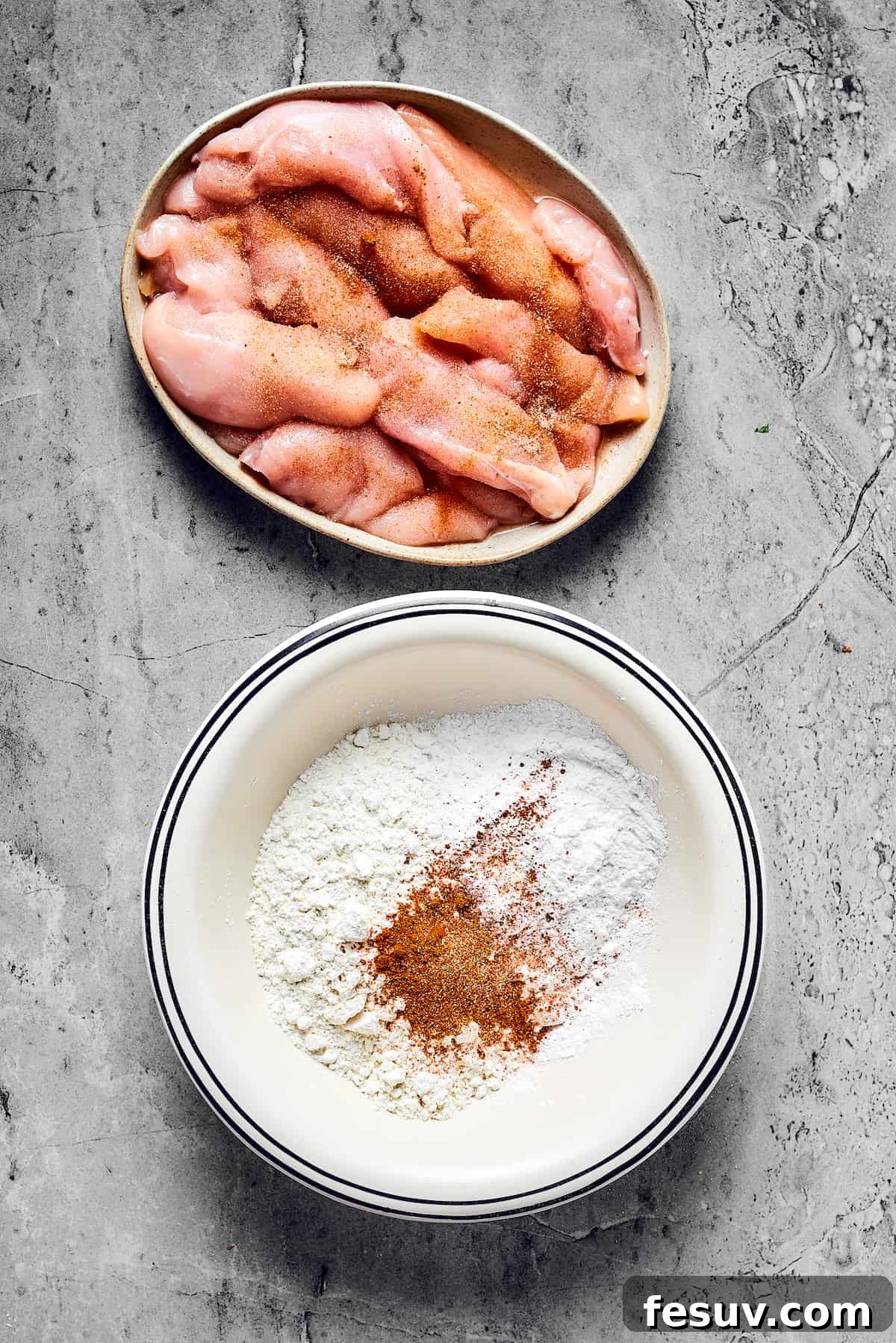 Raw, seasoned chicken strips laid out next to a bowl of dry seasoning mix, preparing for the batter and coating stages.