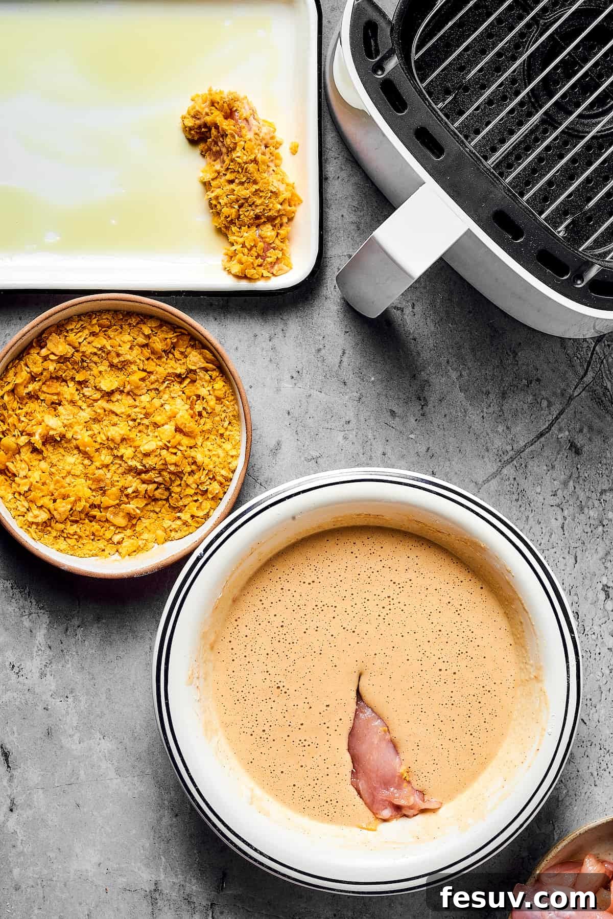 A step-by-step image showing chicken being dipped in batter, then cornflakes, with an air fryer and oiled baking sheet nearby.