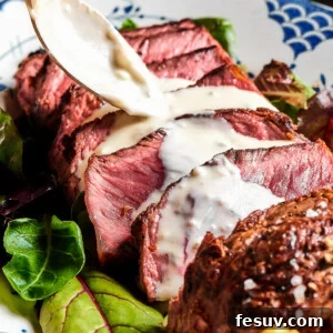 Expertly sliced blue steak with a rich, creamy blue cheese sauce being drizzled generously over the top, showcasing its appealing presentation.