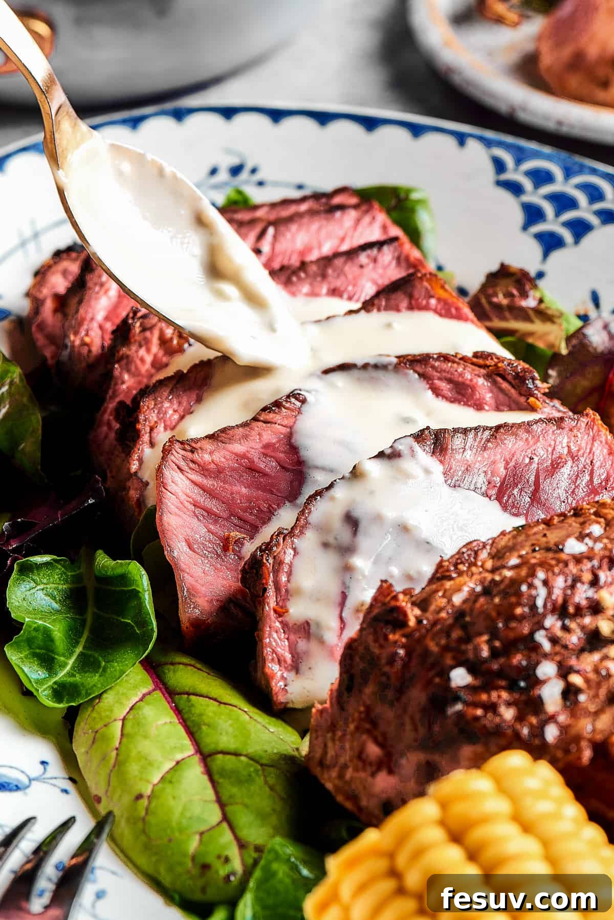 Expertly sliced blue steak with a rich, creamy blue cheese sauce being drizzled generously over the top, showcasing its appealing presentation.