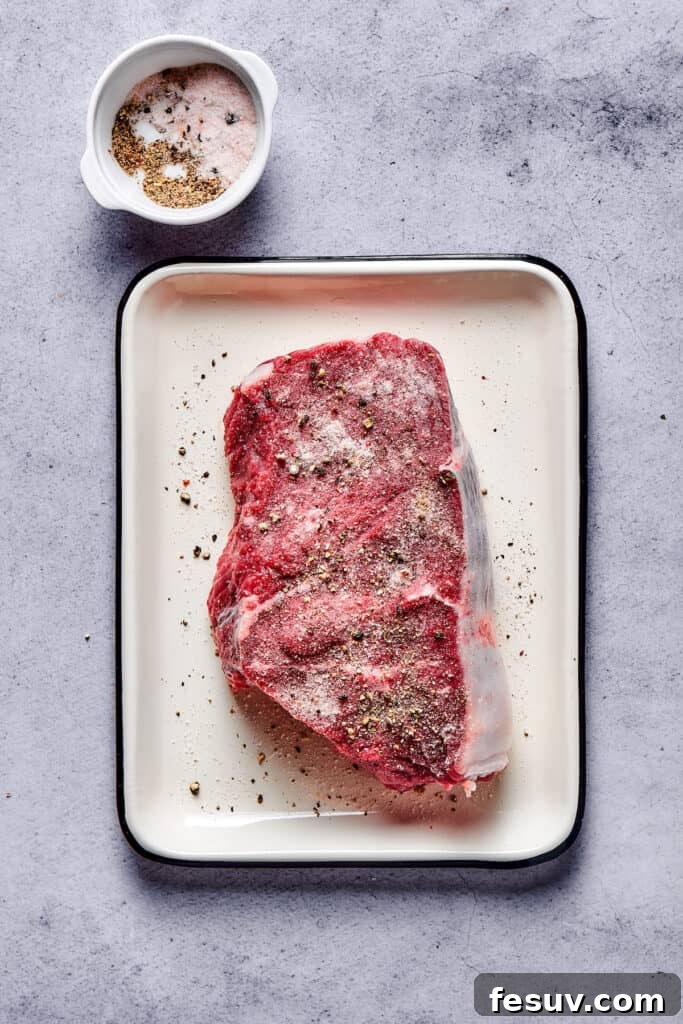 A thick cut of sirloin steak, generously seasoned with coarse salt and freshly ground black pepper, ready for searing in an enamel pan.