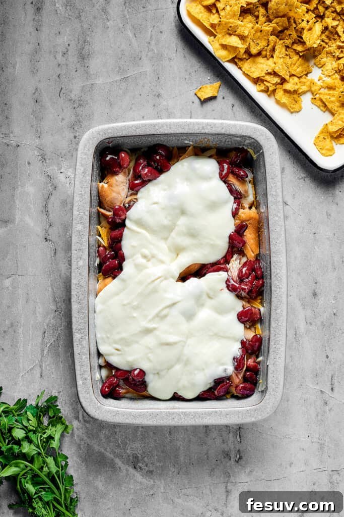 Fiesta Chicken Casserole 8 Beans, white sauce, chicken, and other ingredients layered in a rectangular pan.