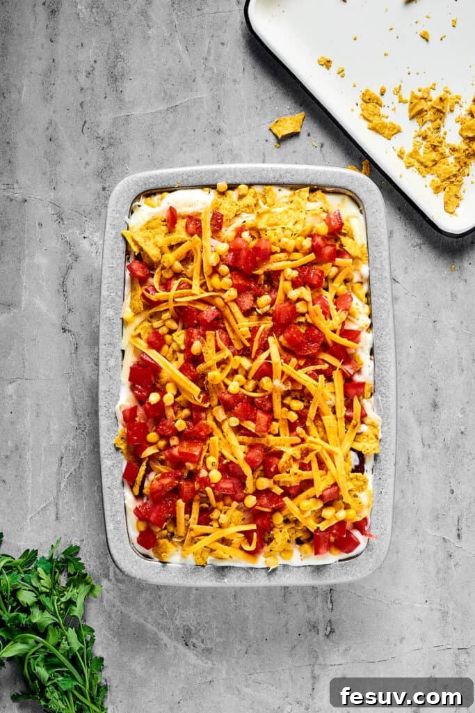 Fiesta Chicken Casserole 10 An unbaked casserole topped with chopped tomatoes and a generous layer of shredded cheese.