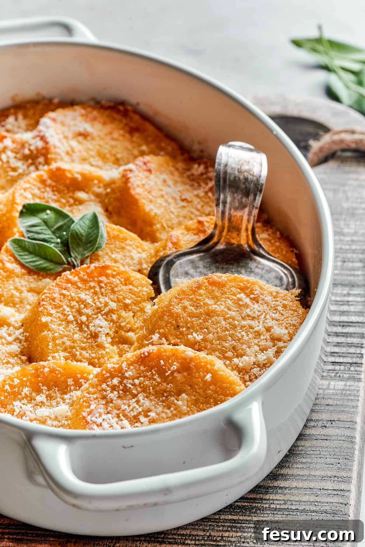 A serving dish of buttered Gnocchi alla Romana with Parmesan, garnished with fresh sage leaves.