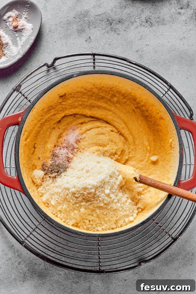 Overhead shot of Parmesan cheese and seasonings being stirred into thick semolina batter.