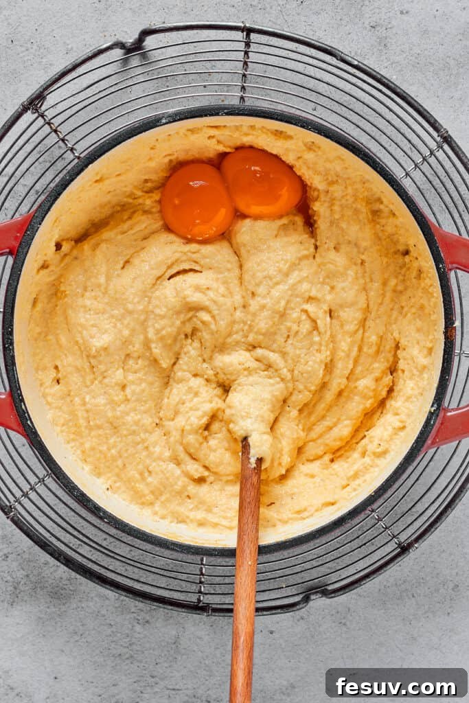 Creamy semolina batter with two egg yolks being stirred in, adding richness.