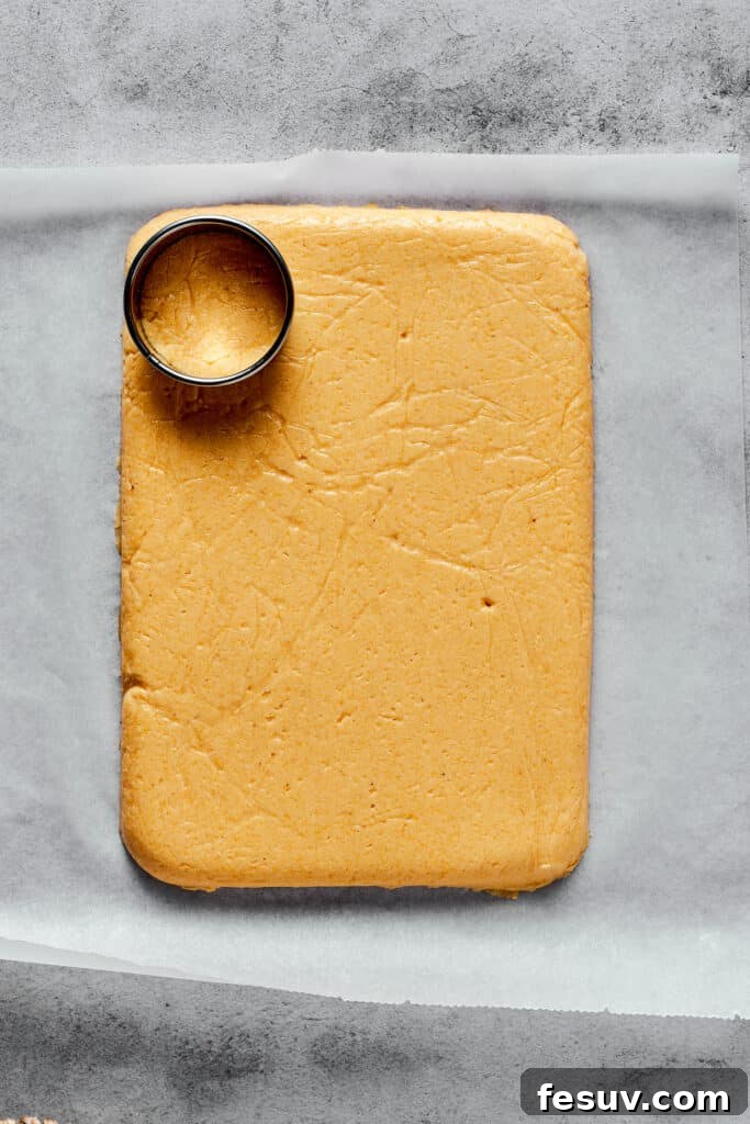 A flat, rectangular sheet of semolina dough on a cutting board, with a circular cookie cutter resting on the dough, ready for shaping.