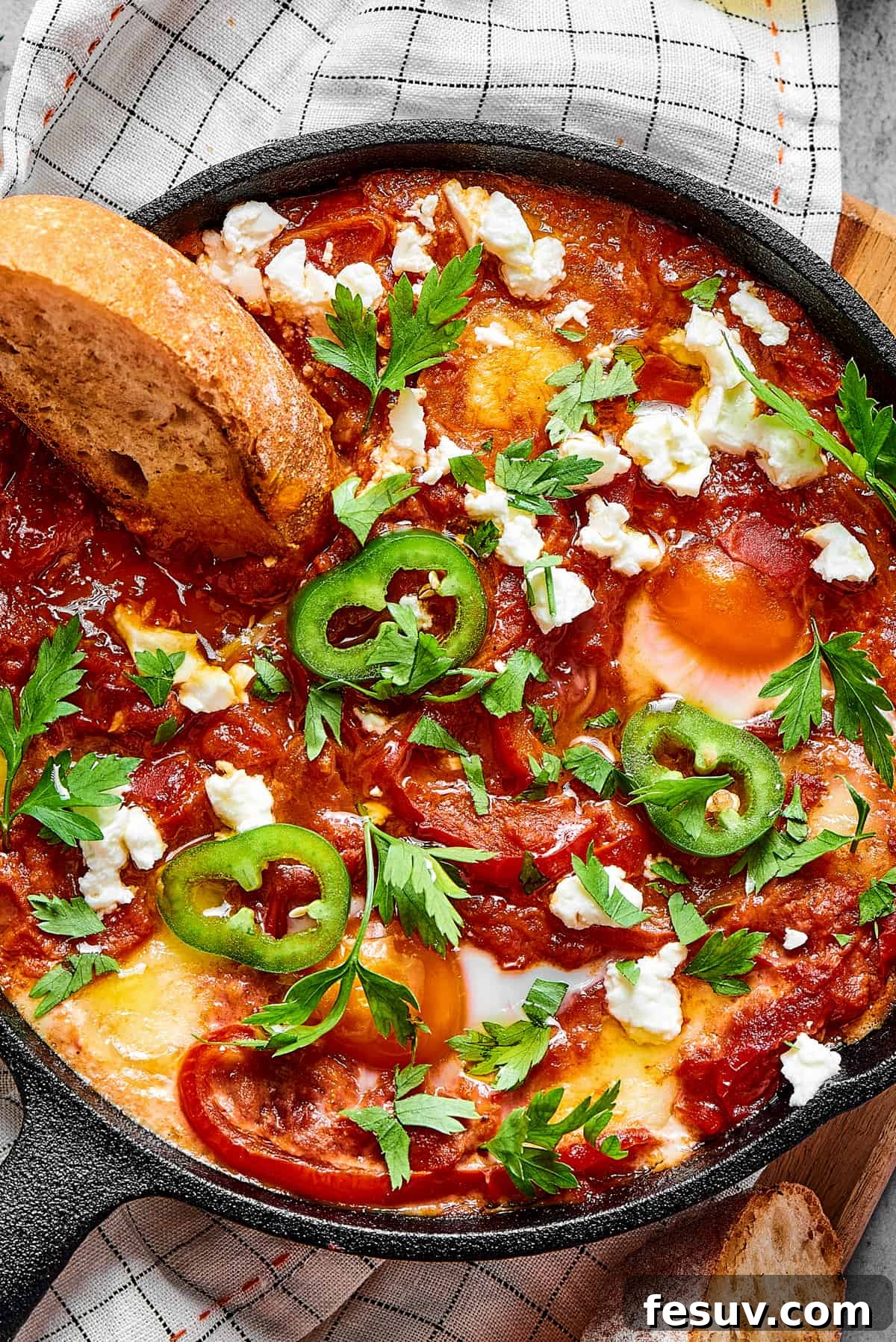 The Ultimate Shakshuka 2 A slice of toasted bread dipped in chunky tomato sauce and poached eggs, garnished with jalapeno and feta cheese.