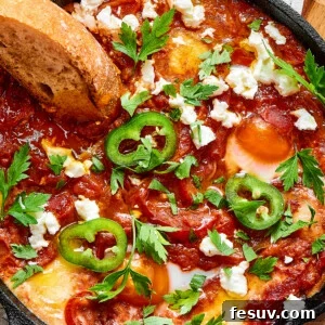 A slice of toasted bread dipped in chunky tomato sauce and poached eggs, garnished with jalapeno and feta cheese.