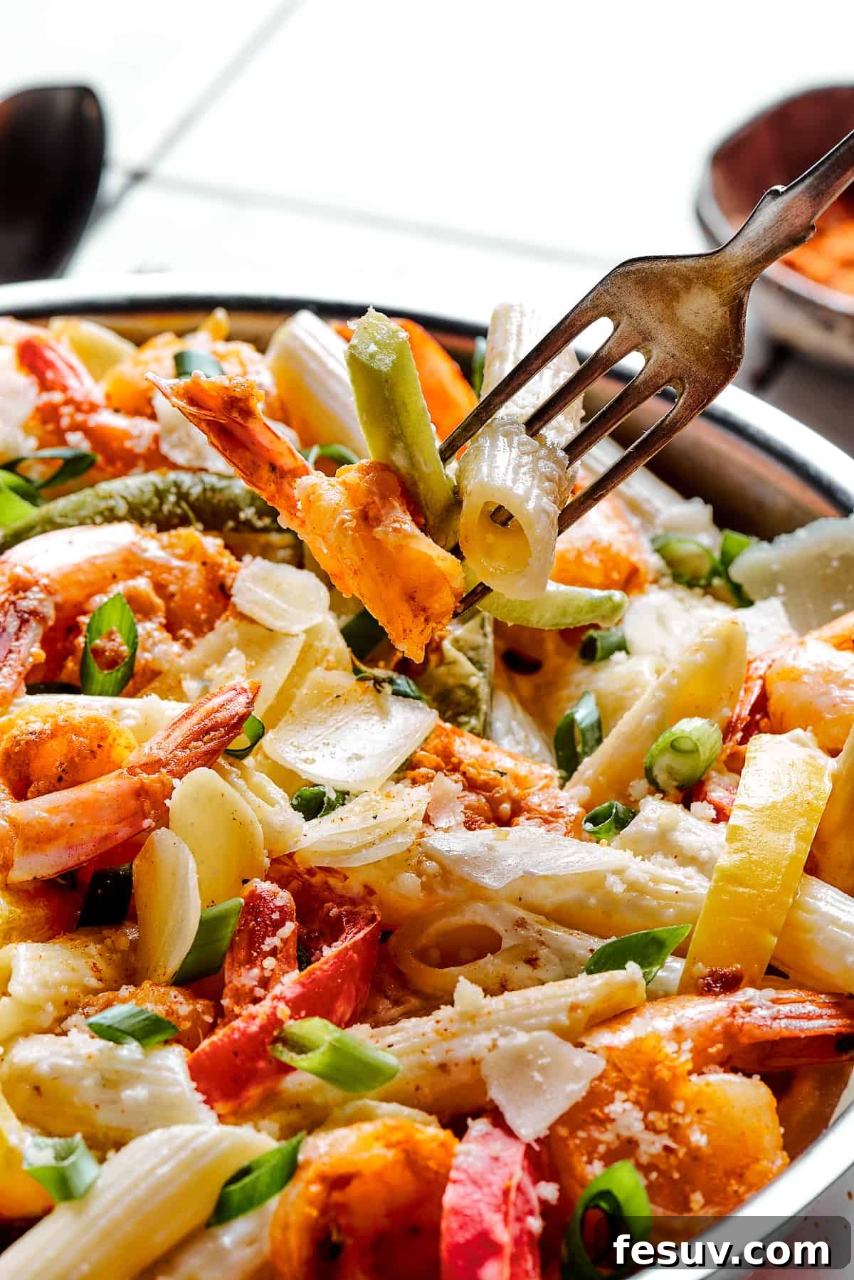 A fork lifting a delicious bite of Rasta pasta, showcasing the creamy sauce, tender penne, plump shrimp, and colorful bell peppers.