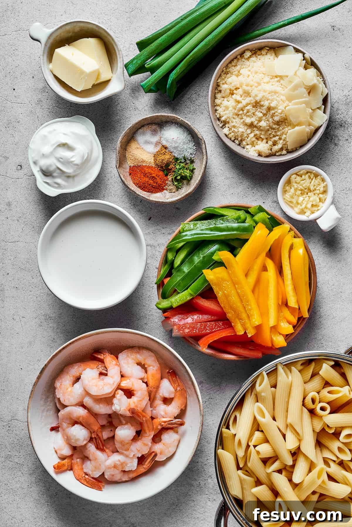 An organized flat lay of all the essential Rasta Pasta ingredients: butter, green onions, Parmesan cheese, cream cheese, various Jamaican spices, minced garlic, heavy cream, thinly sliced red, yellow, and green bell peppers, fresh shrimp, and dry penne pasta.