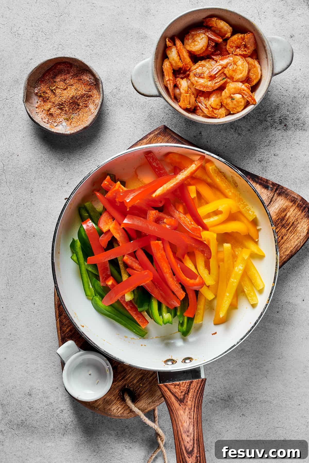 Green, red, and yellow bell peppers sautéing in a hot skillet, placed next to a bowl of perfectly cooked, spicy shrimp.