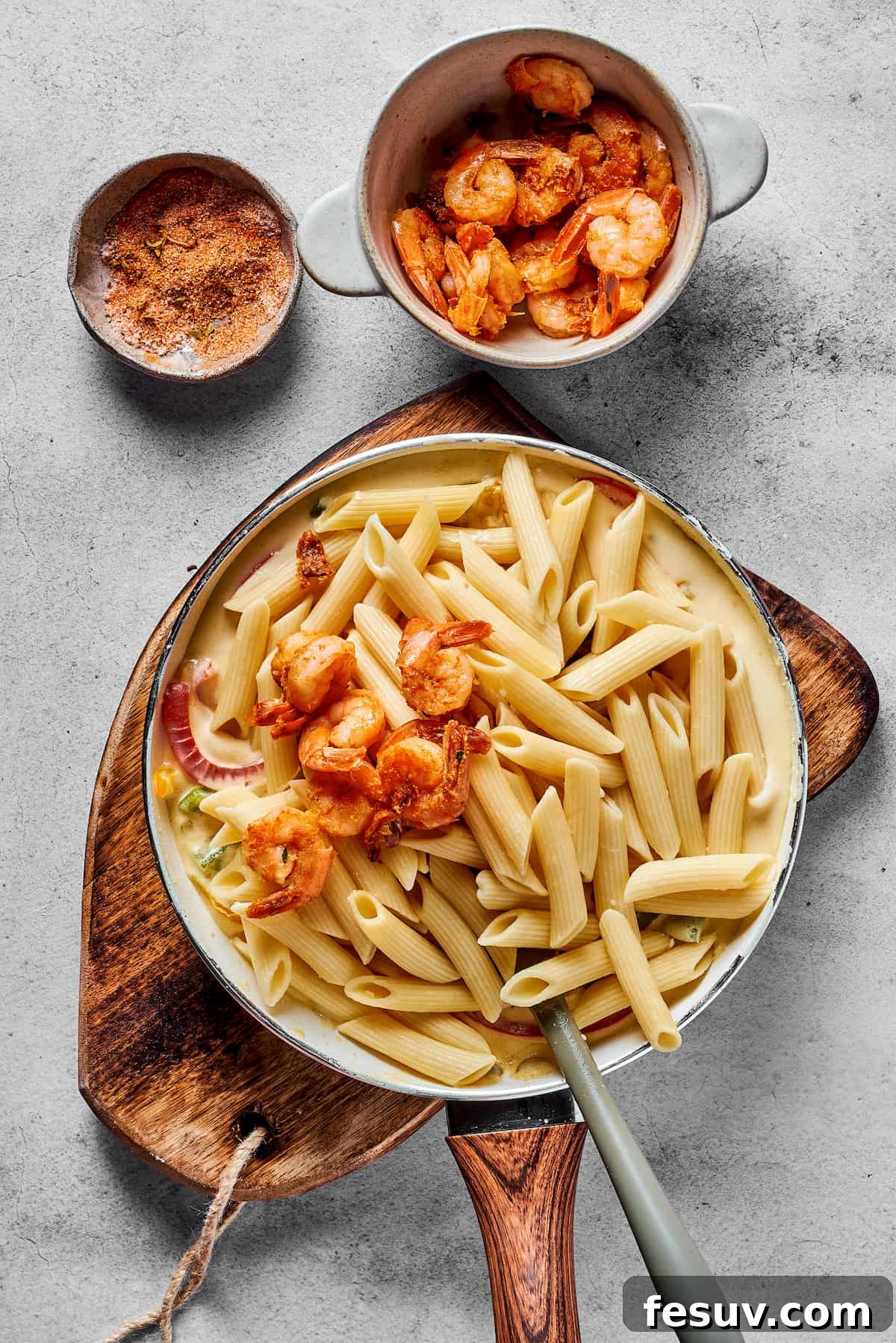 Cooked shrimp and penne pasta being gently mixed into the creamy sauce and bell peppers in a large skillet, ensuring everything is well coated.