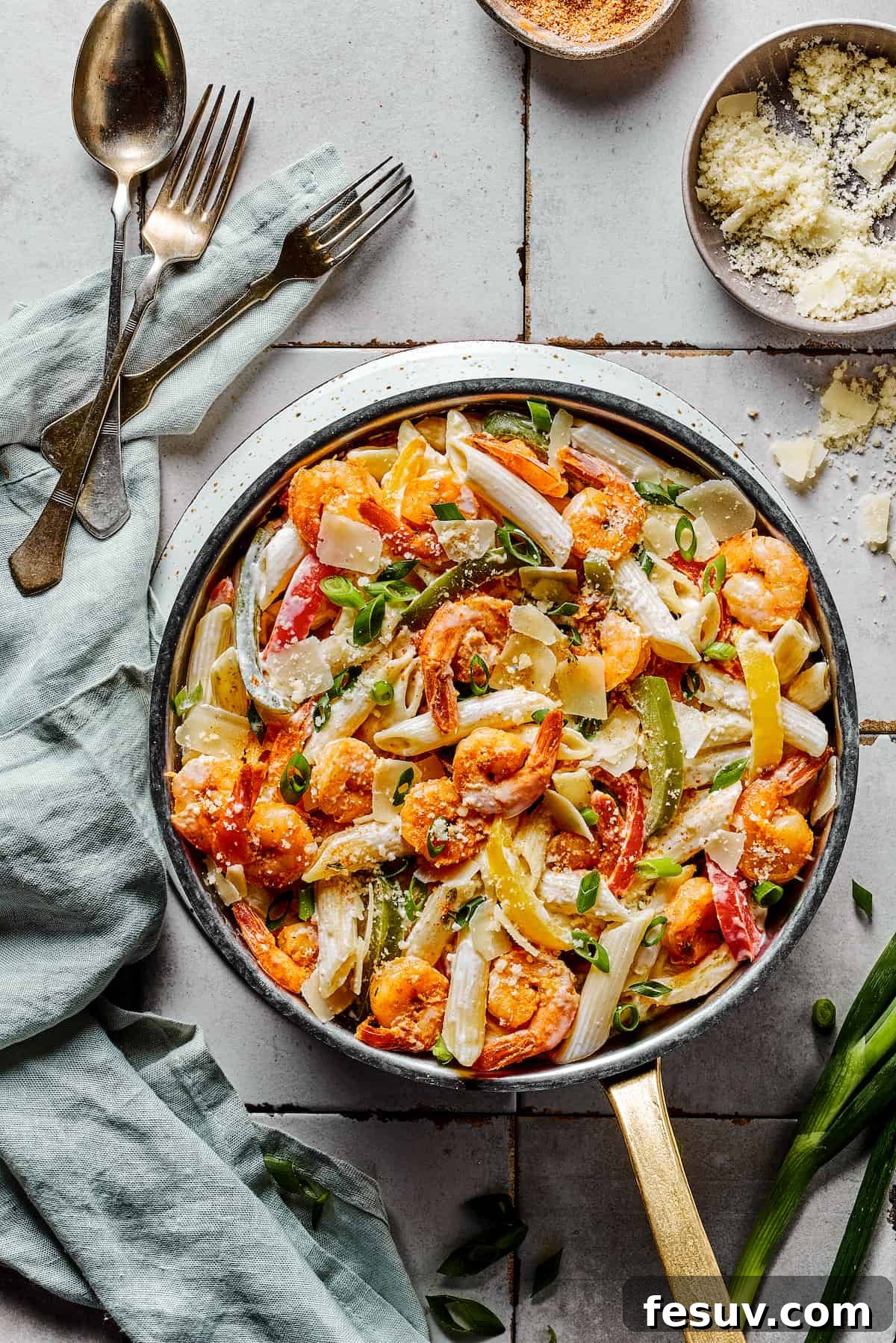 A beautifully presented skillet of Rasta pasta with shrimp, penne, and bell peppers, surrounded by serving spoons, forks, and a cloth napkin, ready for a family meal.