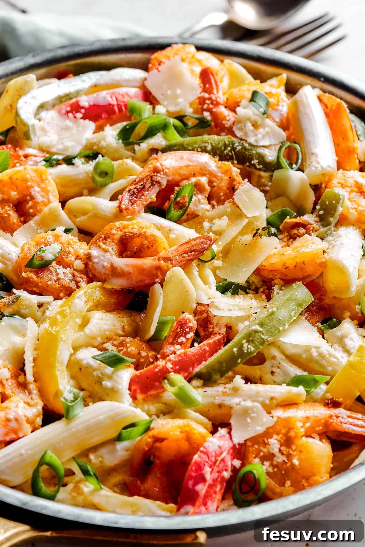 A skillet filled with creamy Rasta pasta, showcasing a harmonious blend of colorful bell peppers, tender penne pasta, and seasoned shrimp coated in a rich, flavorful sauce.