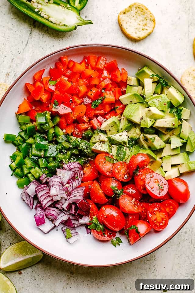 Fresh Ingredients for the Best Homemade Avocado Salsa Close-up shot of freshly diced peppers, jalapeños, tomatoes, avocado, and red onions in a large salad bowl, ready to be mixed for the salsa.
