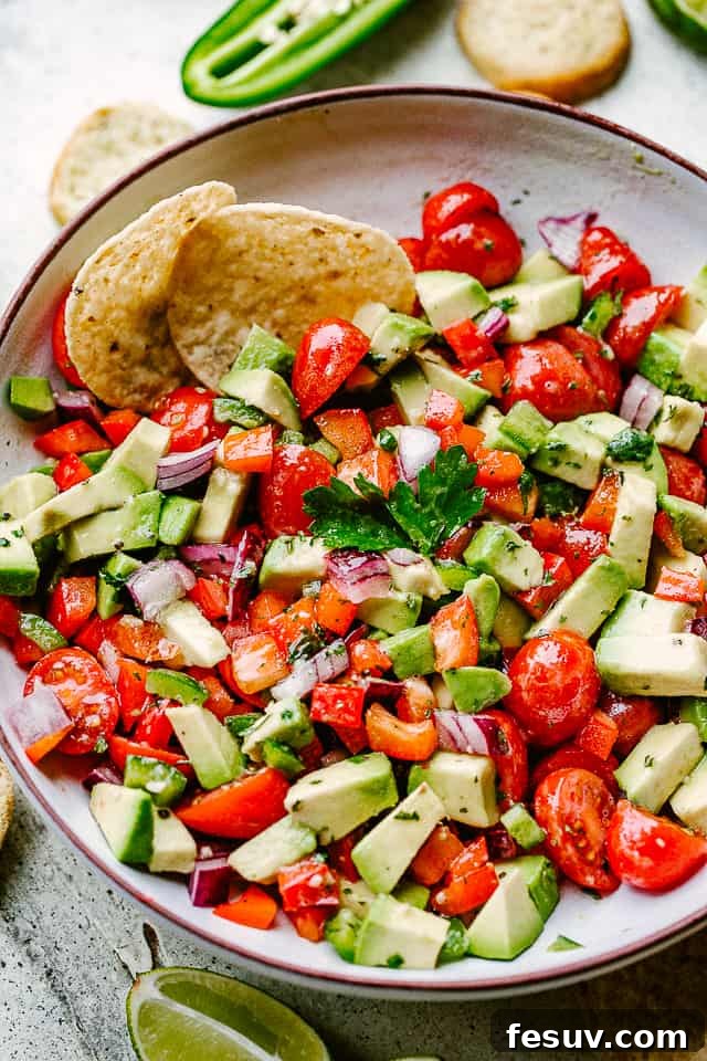 Freshly Prepped Ingredients for Delicious Avocado Salsa A rustic bowl filled with vibrant chopped tomatoes, creamy avocado pieces, and golden tortilla chips, ready for serving.