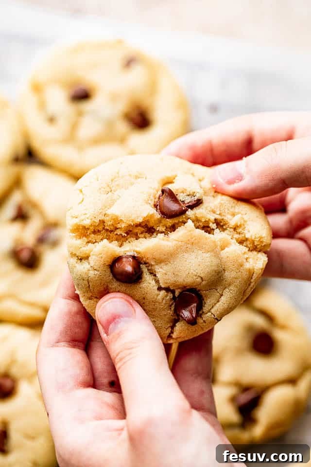 A hand breaking a thick, chewy chocolate chip cookie in half, showcasing its warm, inviting texture and generous pockets of melted chocolate. Ideal for sharing or enjoying a perfect bite.