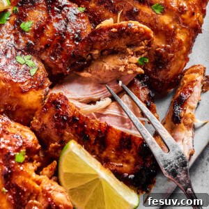 A platter of grilled chicken, with one piece being pulled apart by a grilling fork to show the texture of the interior.